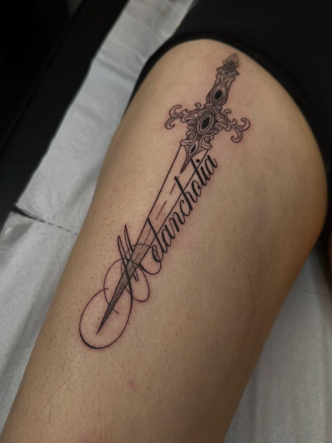 Tatouage dague et lettrage Melancholia sur la cuisse — petale.ttt