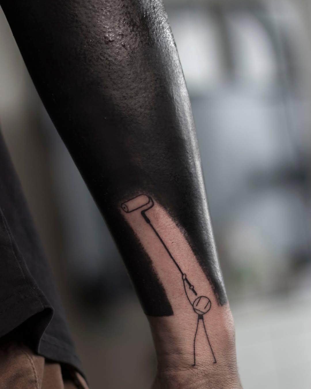 Tattoo of a paint roller with stick figure on forearm, cover-up