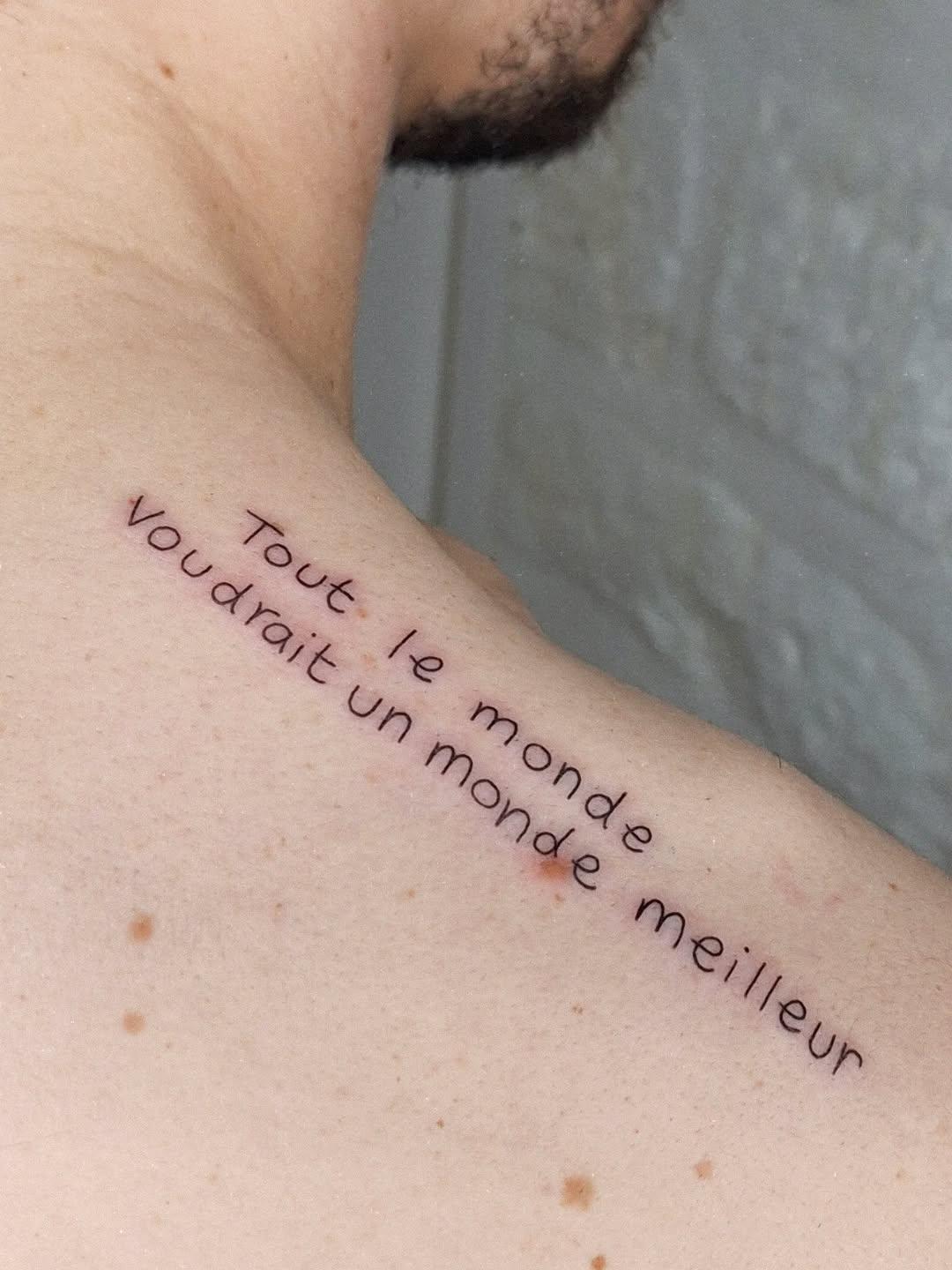 Fine line text tattoo on trapezius — Tout le monde voudrait un monde meilleur